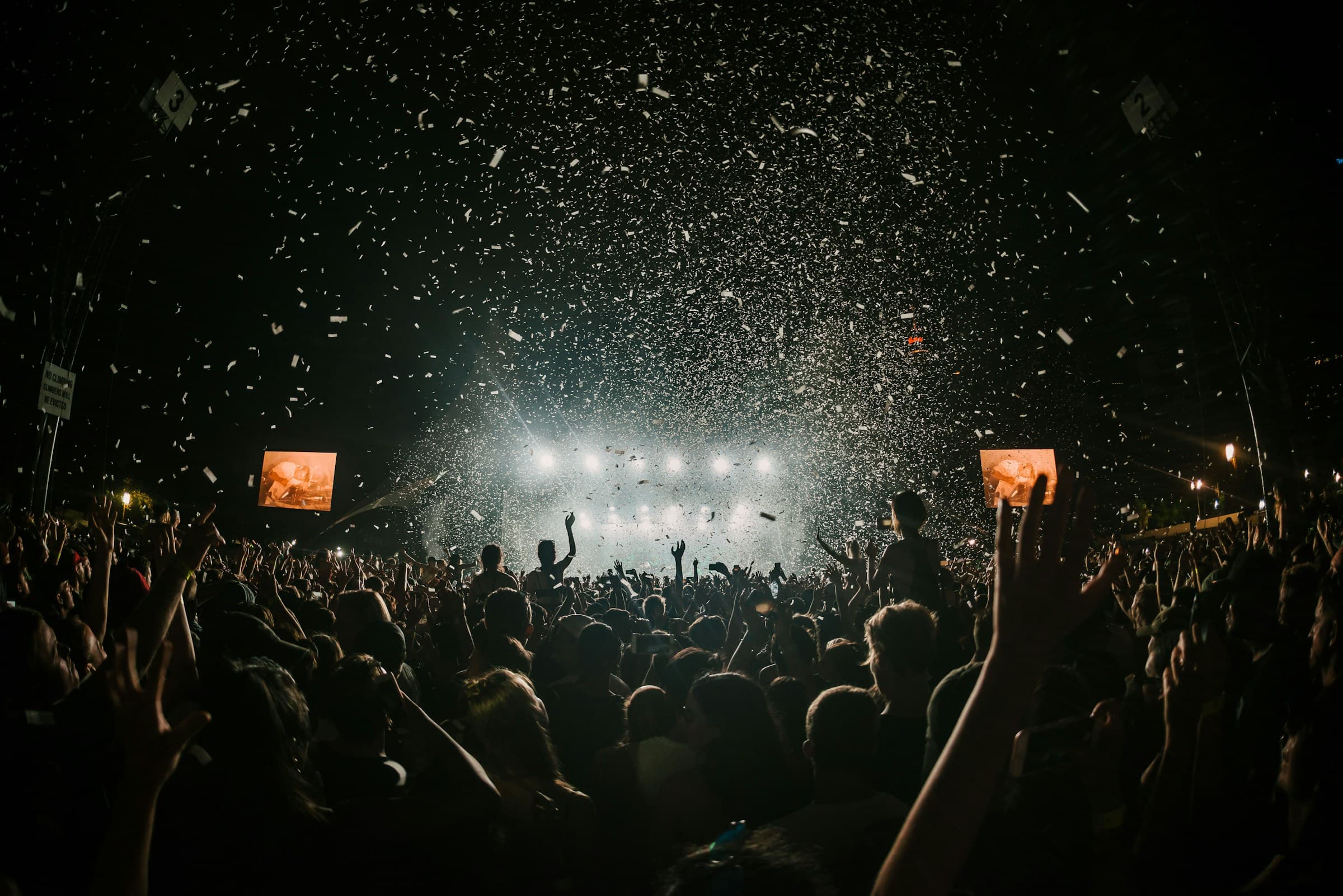 A festival crowd raising their hands as confetti falls under the stage lights