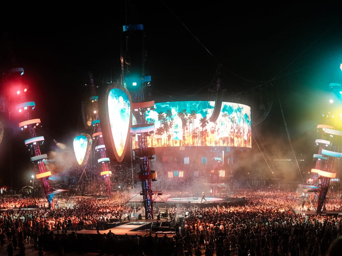 A crowd facing a colorful stage light show at an outdoor night concert