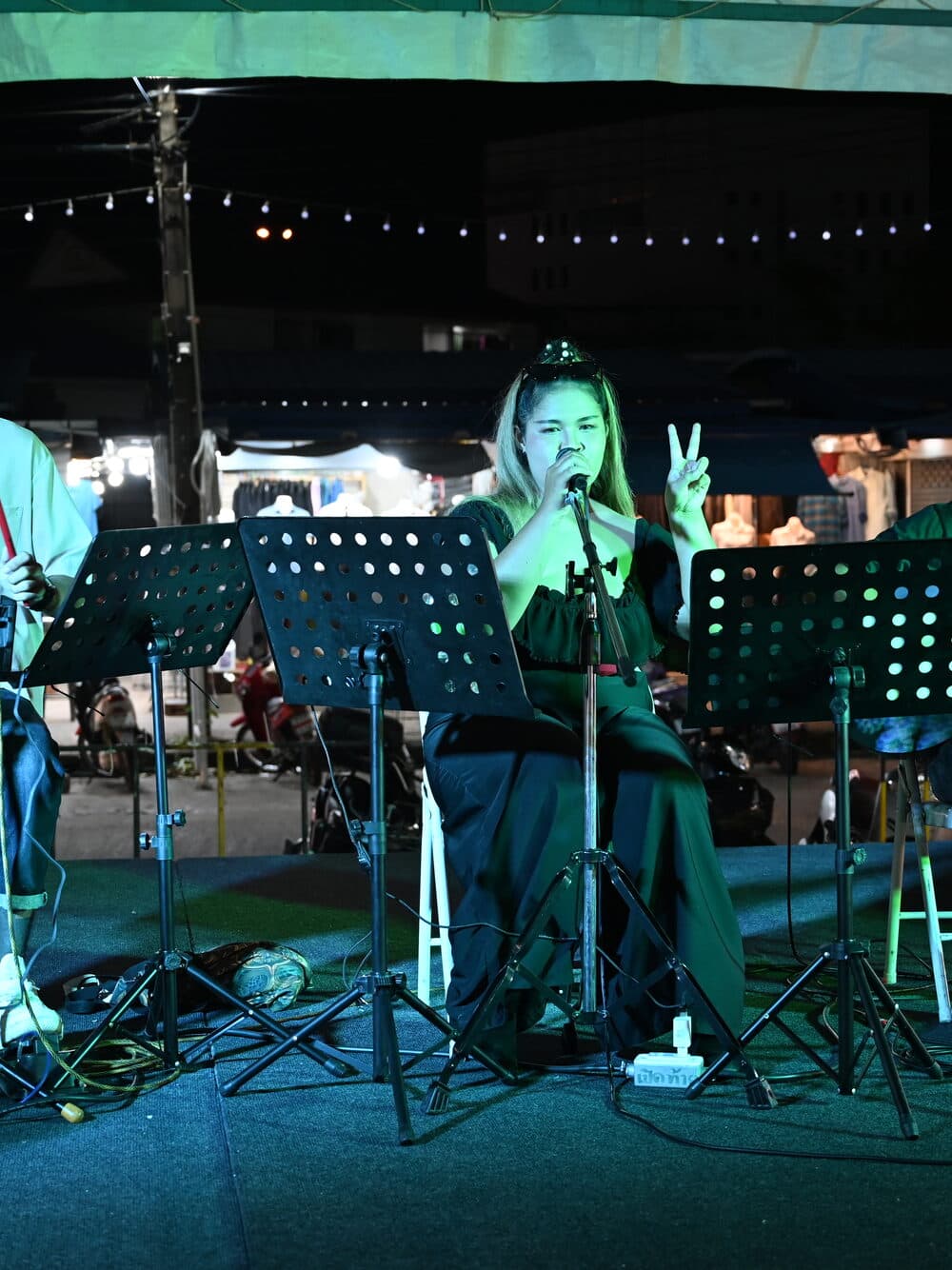 A singer performing at a small outdoor night stage strung with lights