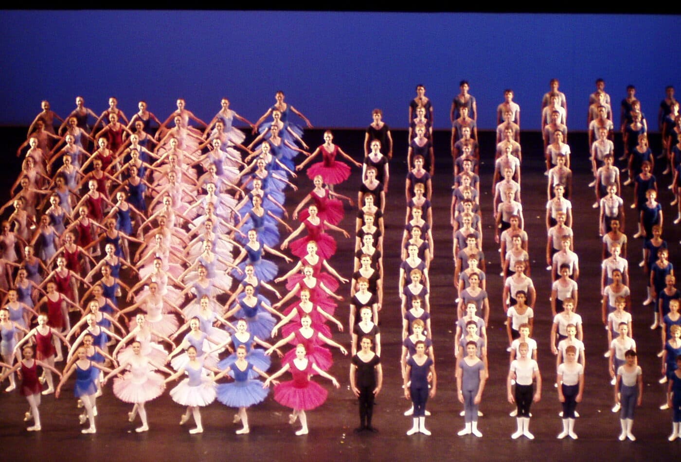 Rows of dancers in colorful costumes lined up on a theatre stage
